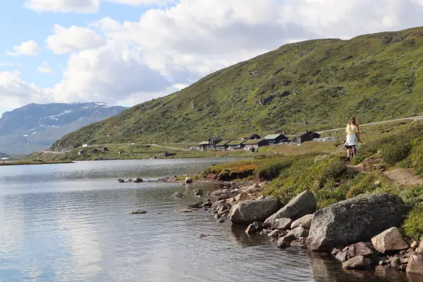 Sommer på Haukeliseter, to personer går langs med vannet i et frodig sommer terreng, Haukeliseter fjellstue i bakgrunnen