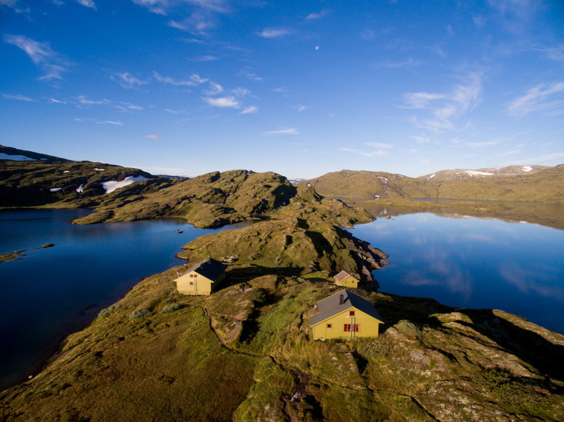 to grønne hytter med et lite vann på hver side, ligger i et fjellandskap