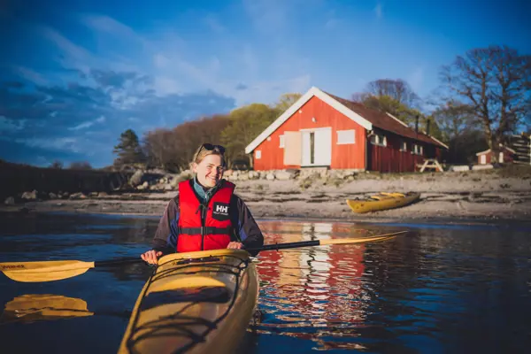 En jente som padler i kajakk utenfor en hytte