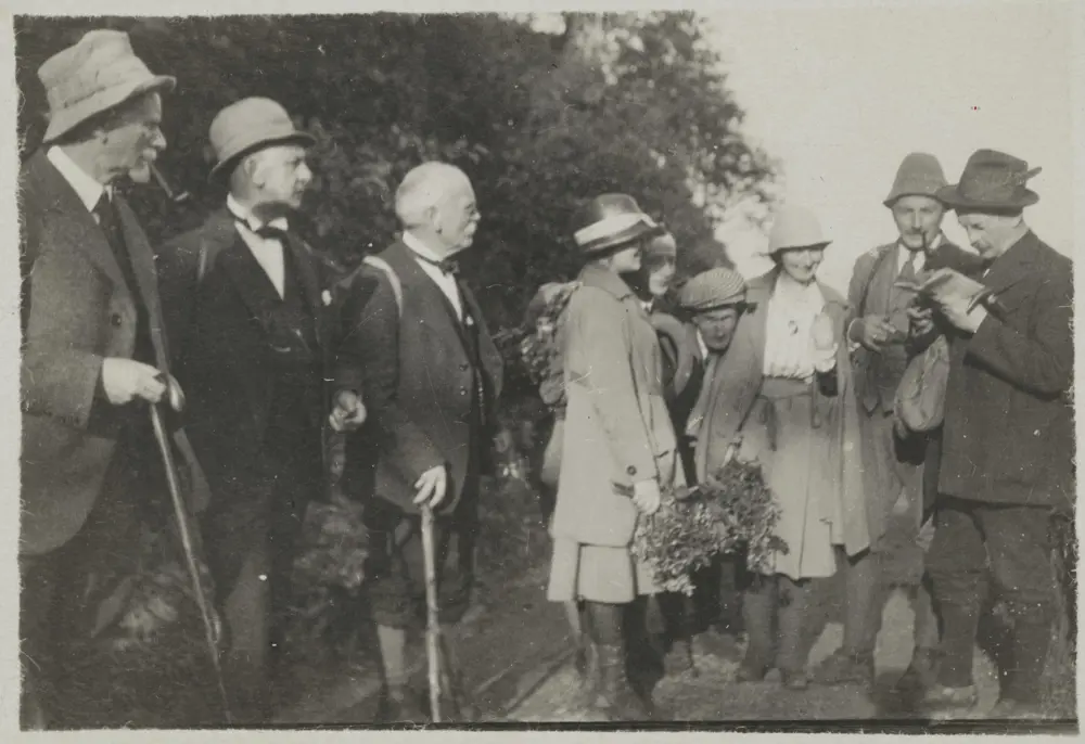Historisk foto i svart-hvitt av pent kledde menn og kvinner på tur.