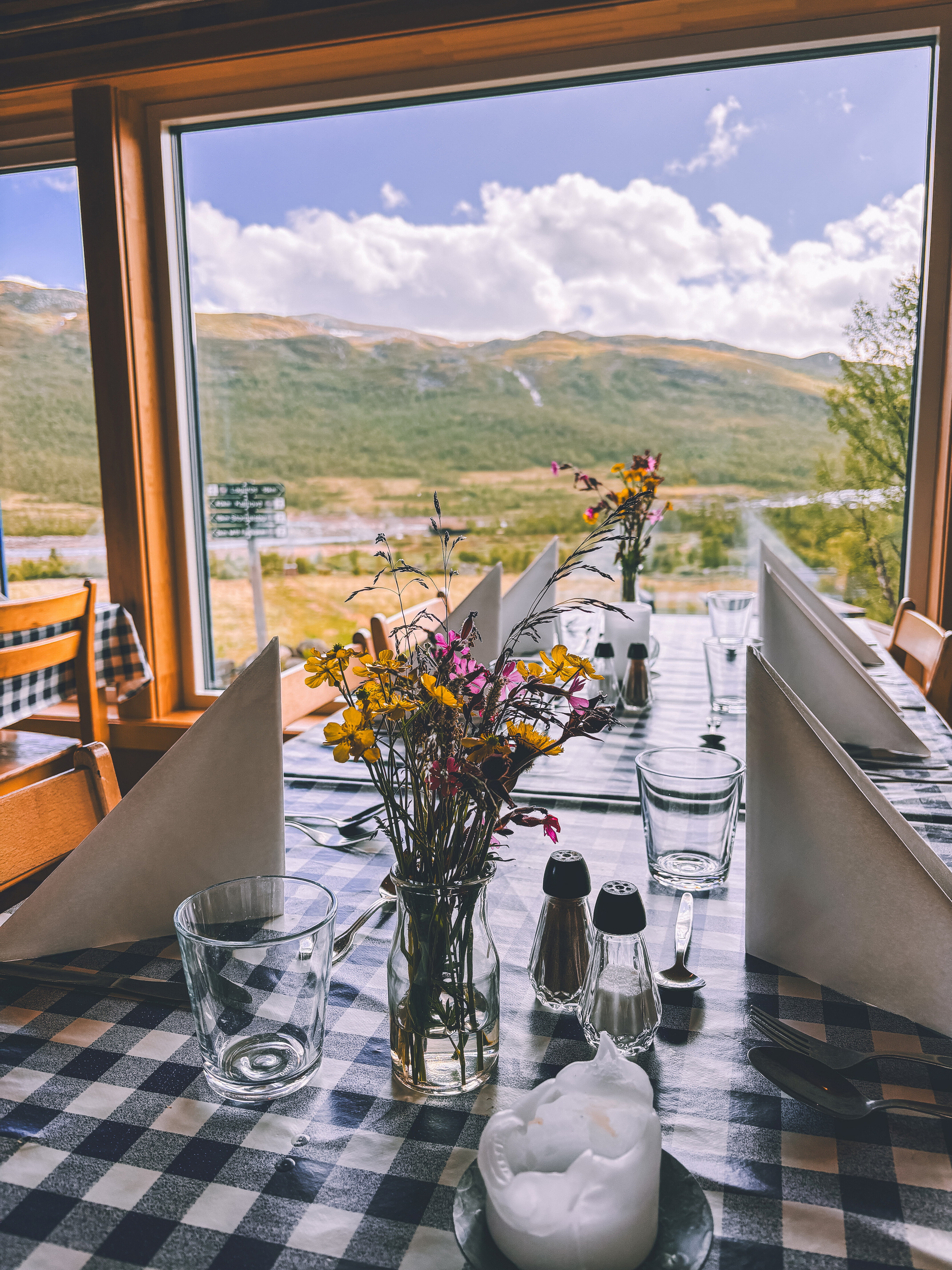 bilde fra innsiden av et hus hvor det er dekket p&aring; med blomster og servietter p&aring; bordet, og med utsikt ut p&aring; naturen. 