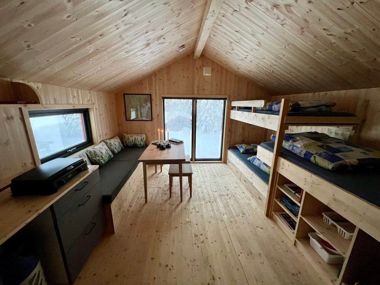 Innsiden av en hytter hvor det står en køyeseng, en sofa og i enden er et stort vindu.