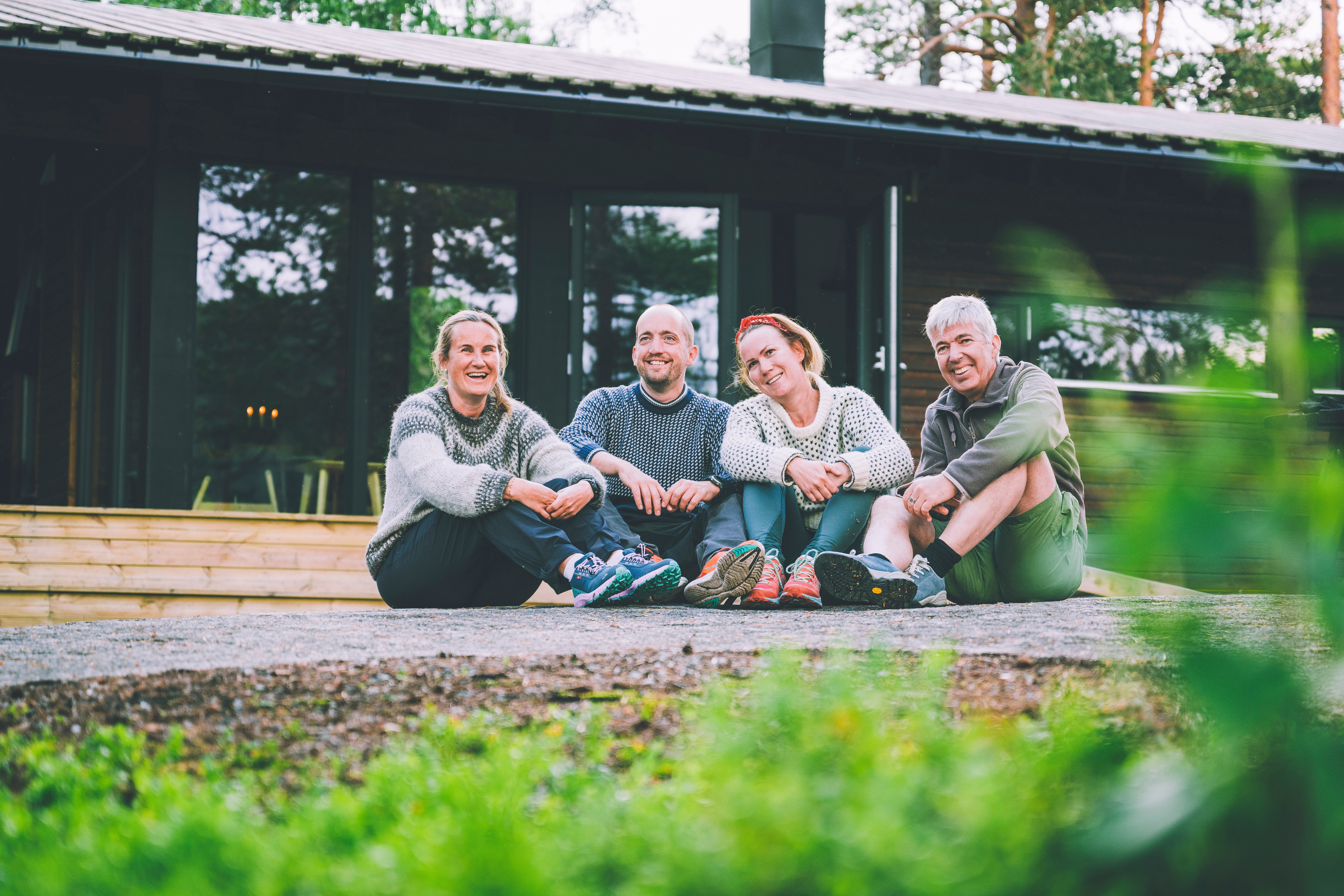 Fire turfolk sitter utenfor Damslett, en moderne ubetjent turisthytte i skogen.