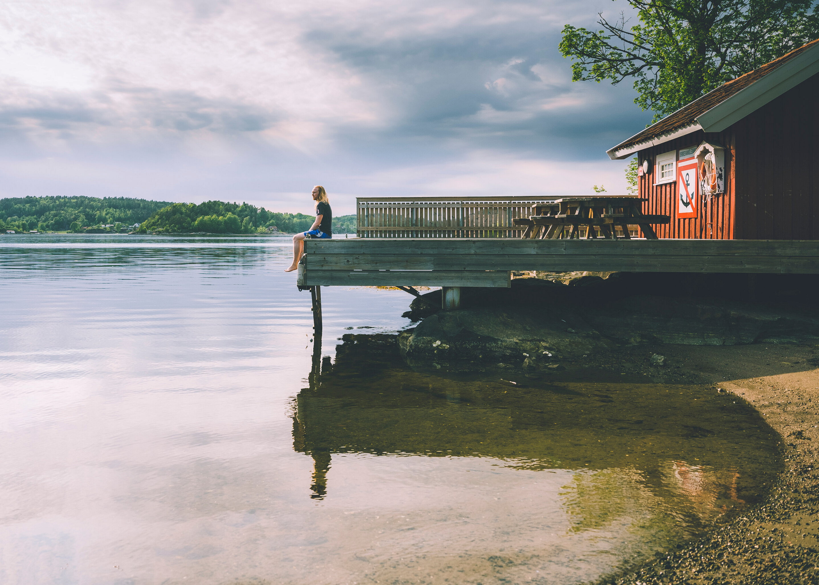 mann som sitter utterst p&aring; en brygge en sommerdag