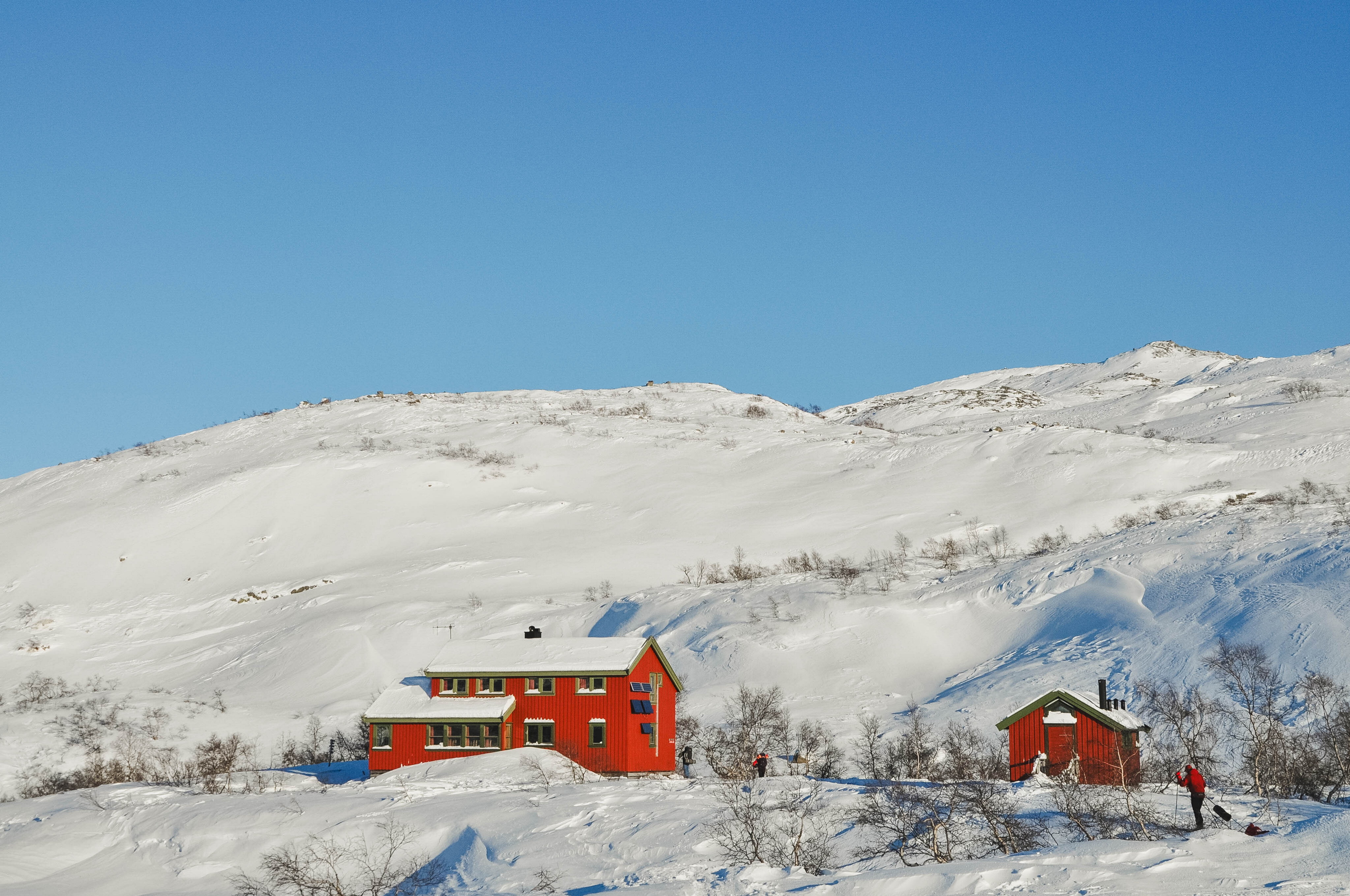 En r&oslash;d stor hytte med gr&oslash;nne karmer i sn&oslash;dekte fjellomr&aring;der.