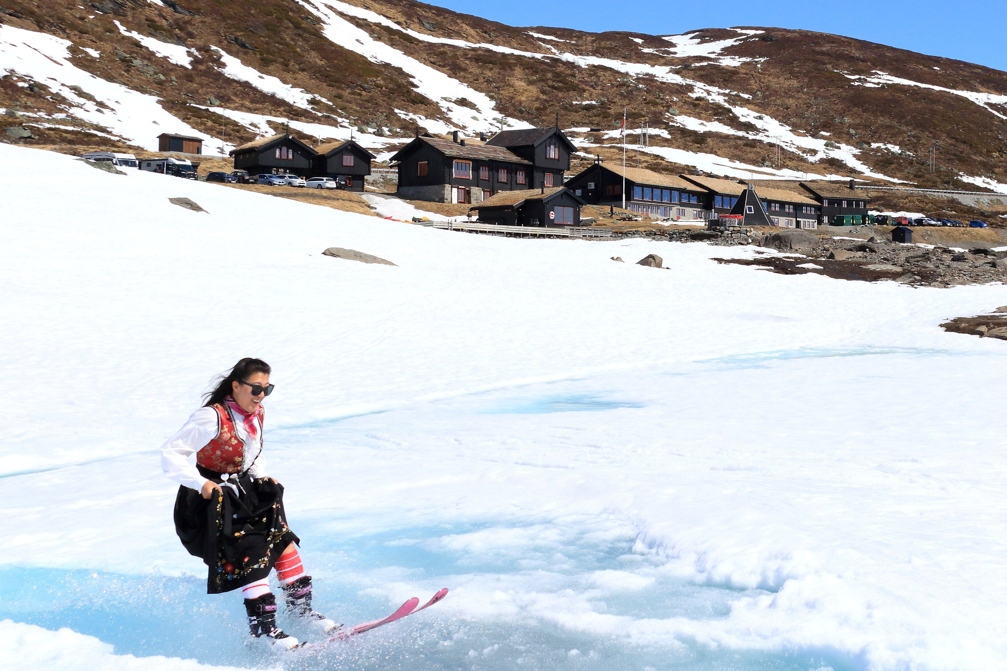 Foto. En dame st&aring;r p&aring; ski i bunad, Haukeliseter i bakgrunnen