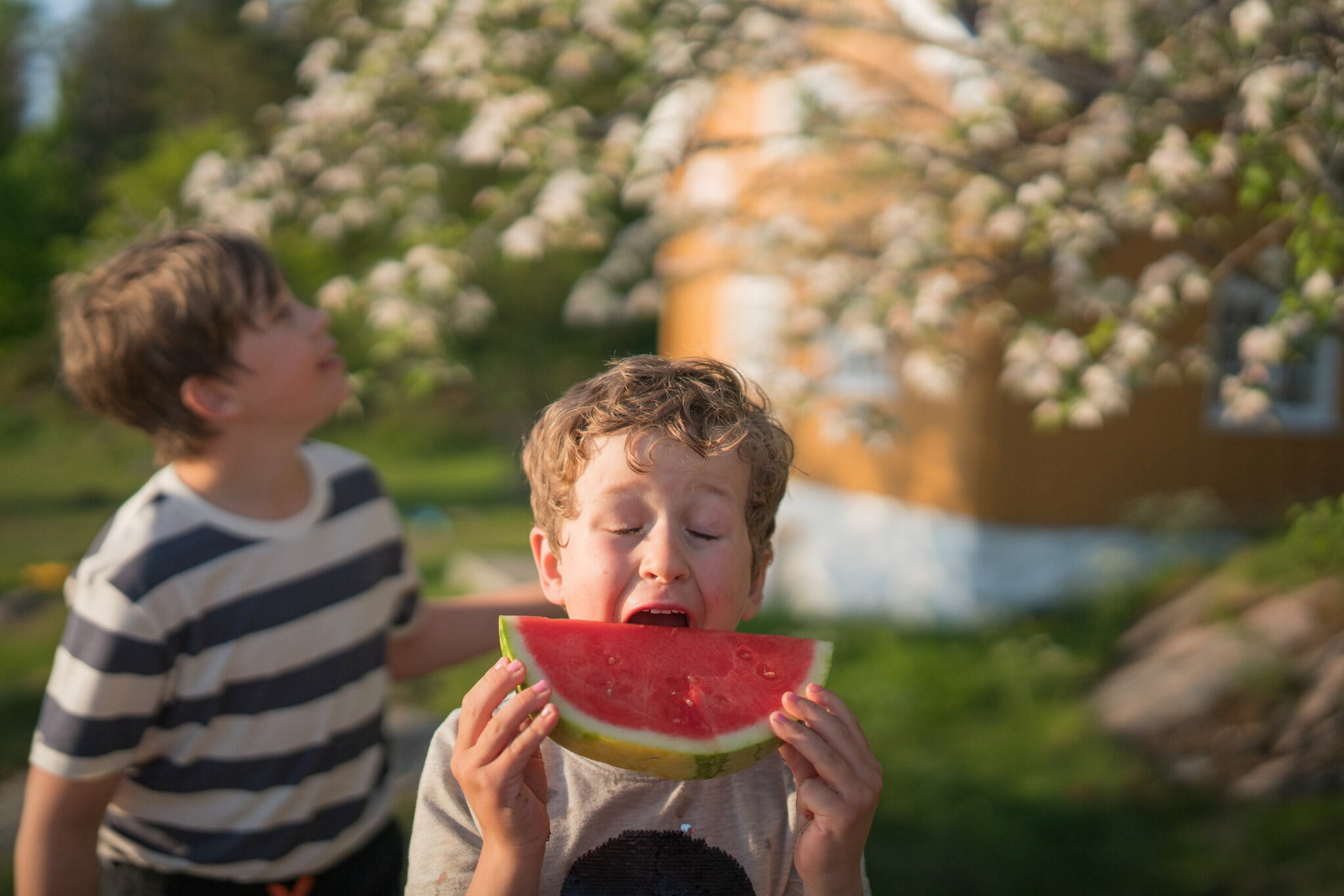 Barn spiser melon foran gul hytte