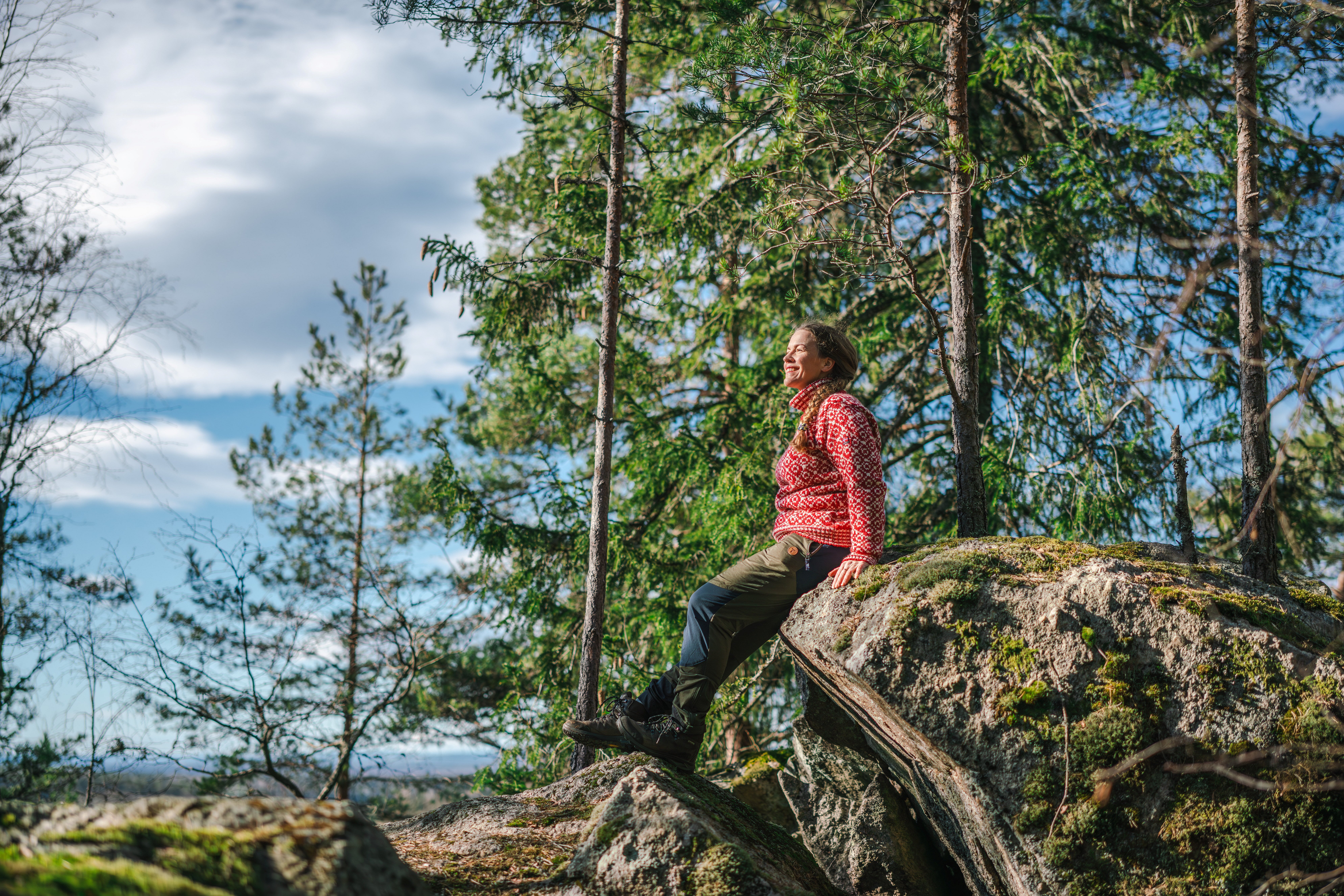 person som sitter ute i skogen p&aring; en liten fjellknaus