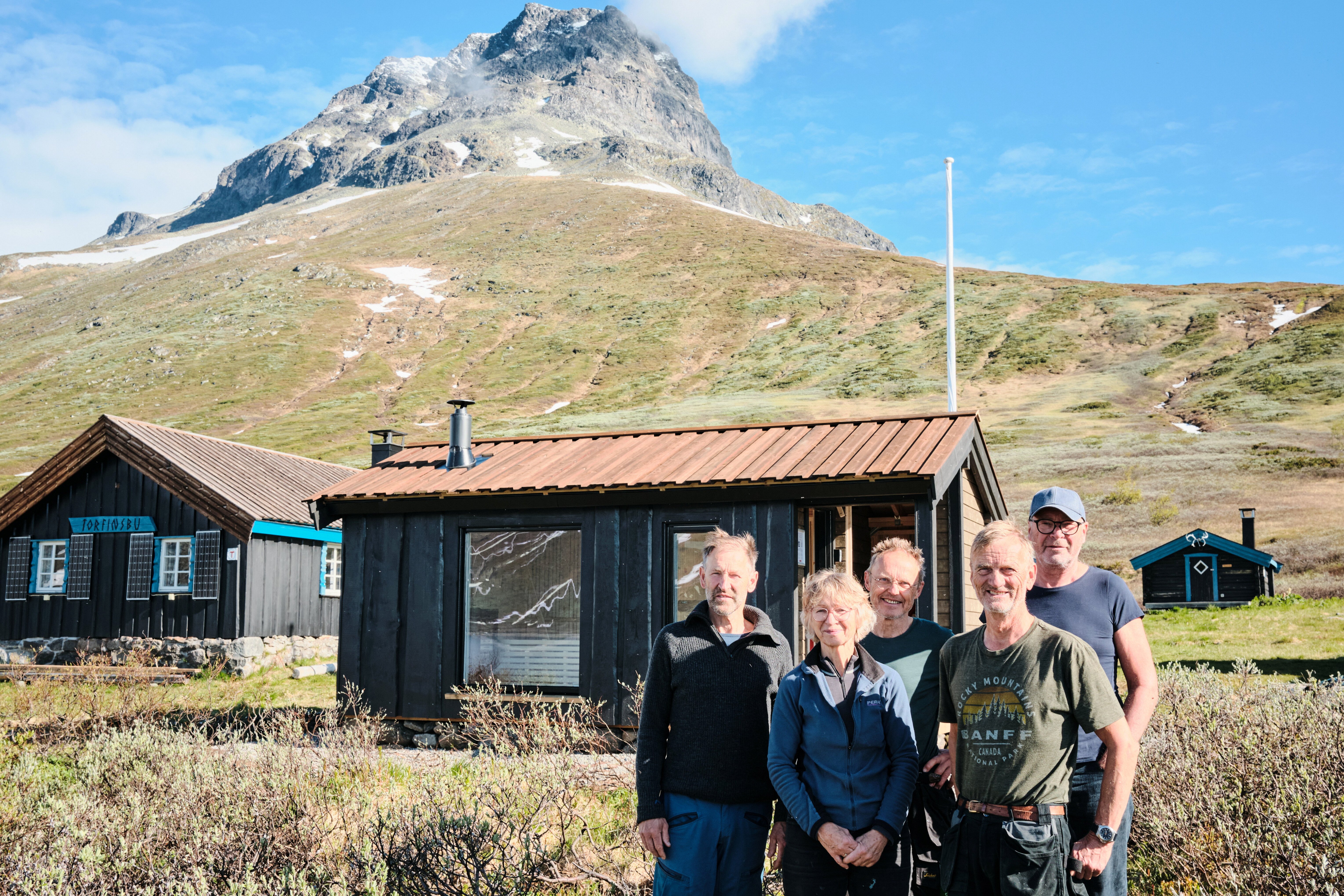personer som st&aring;r foran en badstue med fjell og hytter rundt