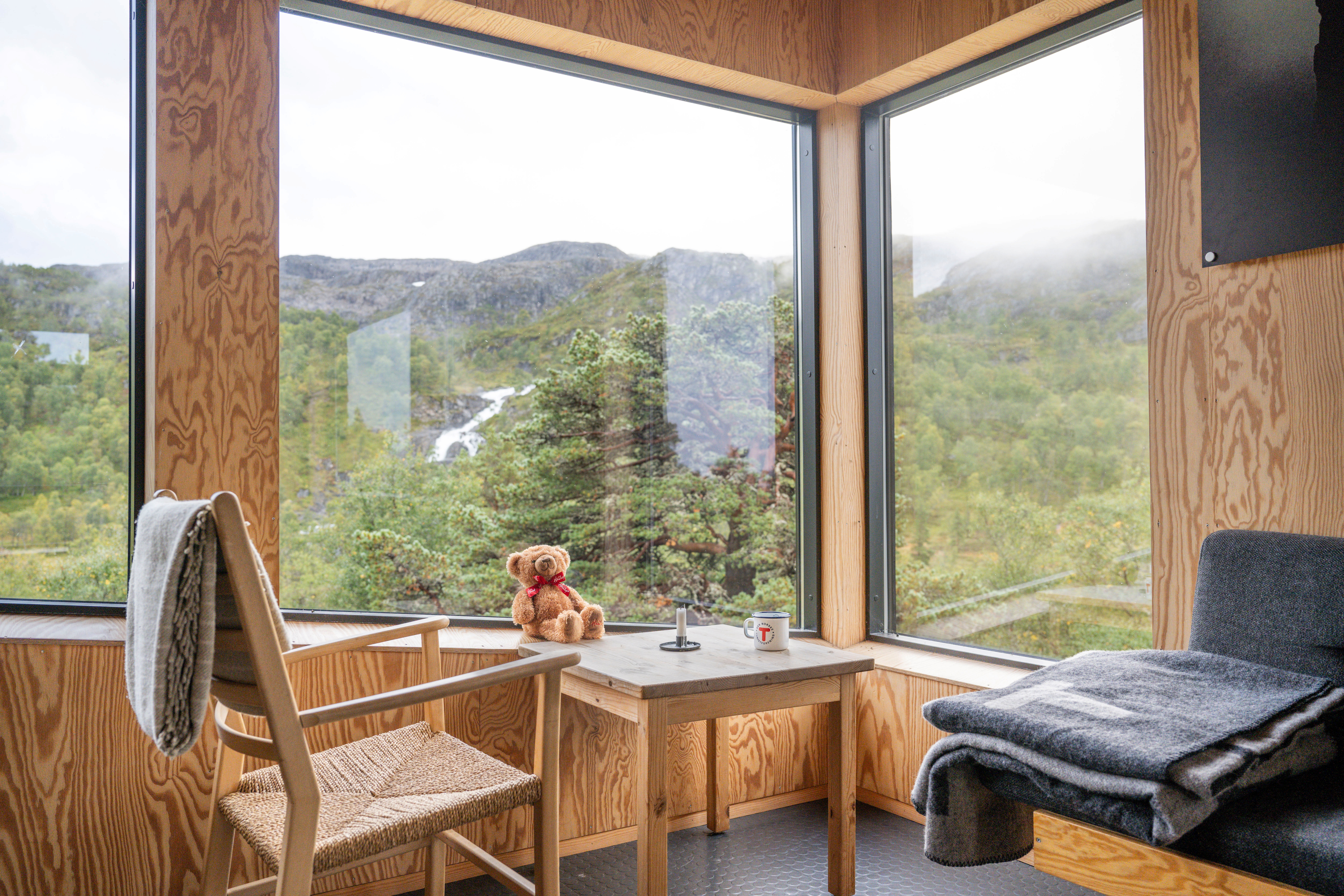 bilde av en sittegruppe ved store panoramavinduer hvor man ser ut p&aring; skog