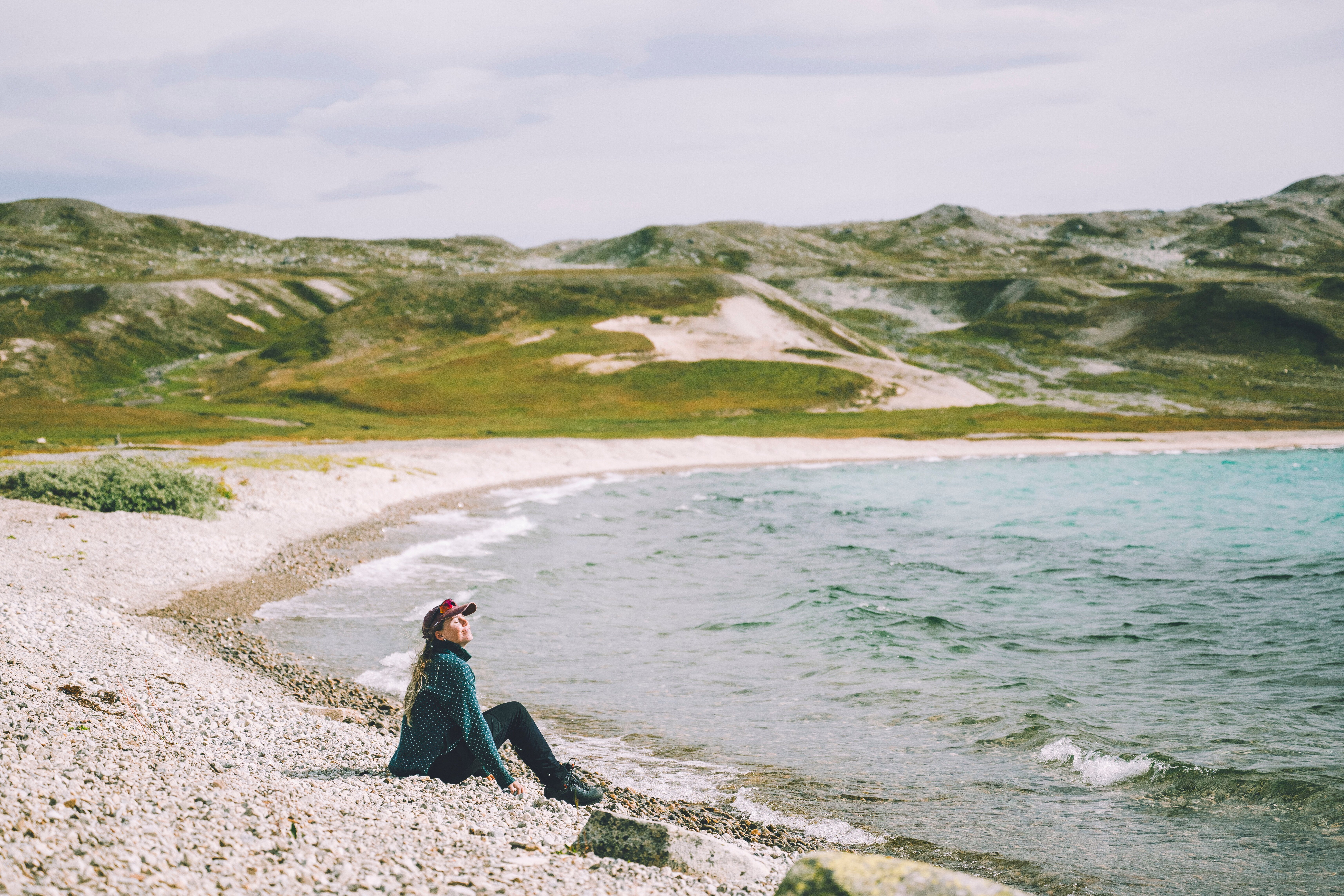 Kvinne sitter p&aring; strand p&aring; fjellet