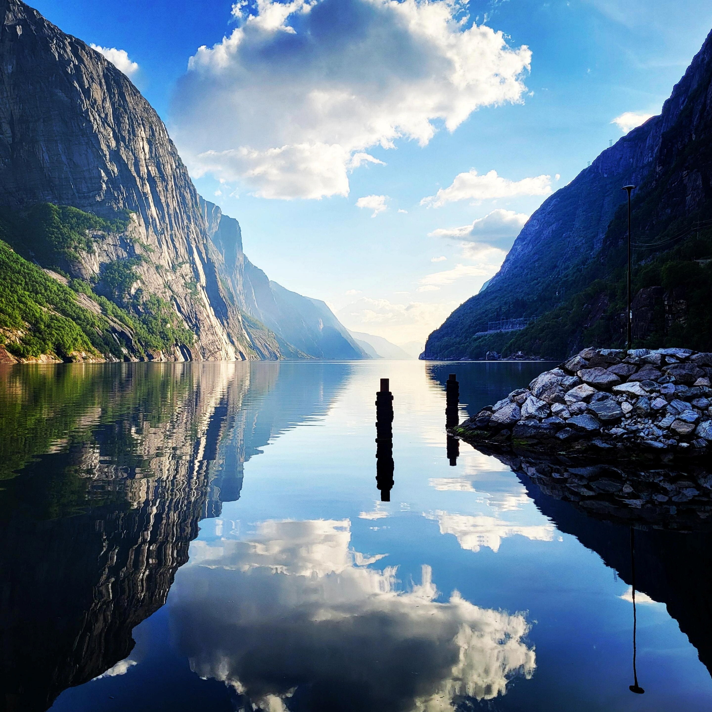 Bilde av en speilblank fjord med fjell p&aring; sidene.