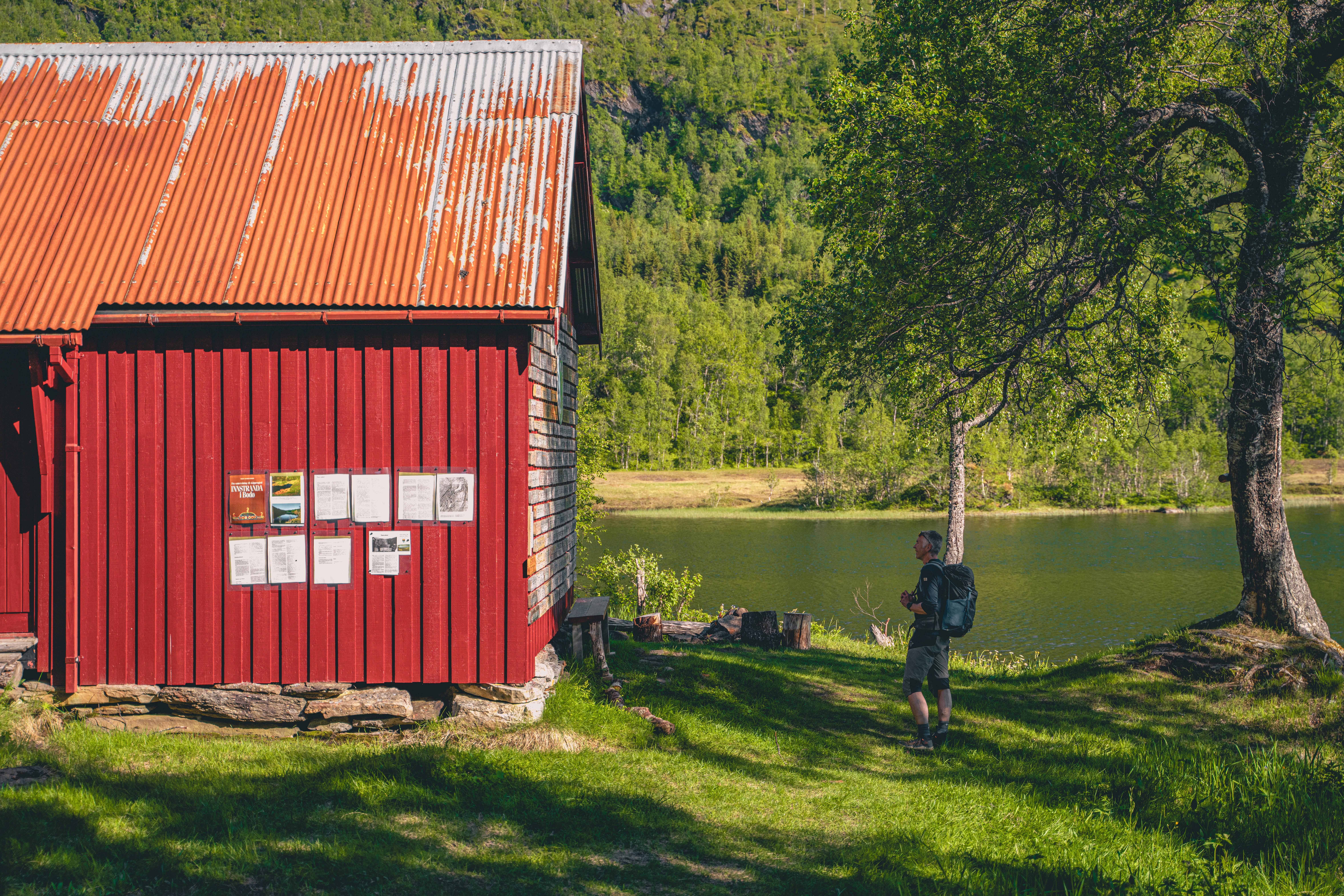 bilde av en mann som st&aring;r foran et vann, hvor man ser litt av et r&oslash;dt bygg