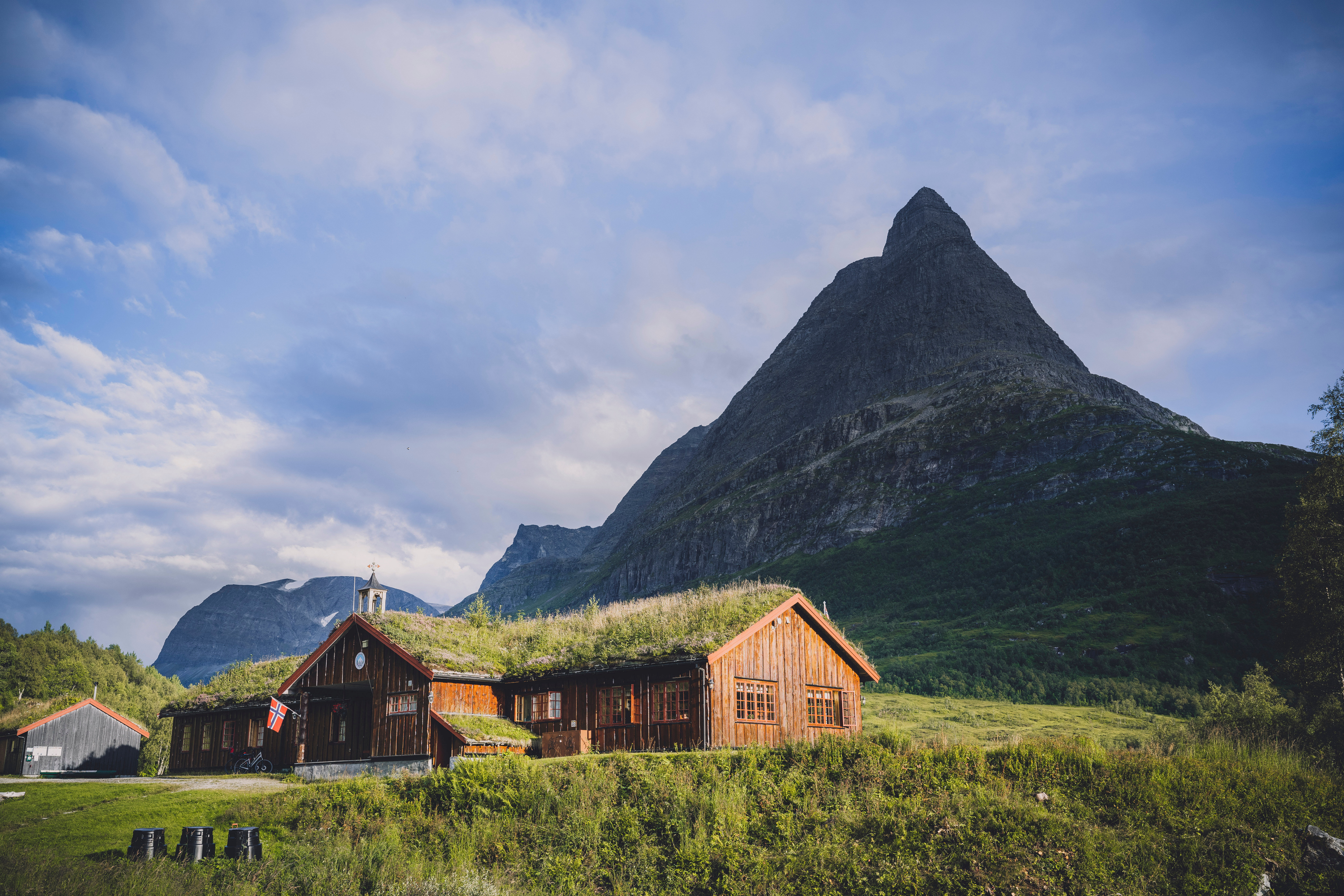 en koselig hytte med torvtak, bak er et spisst fjell