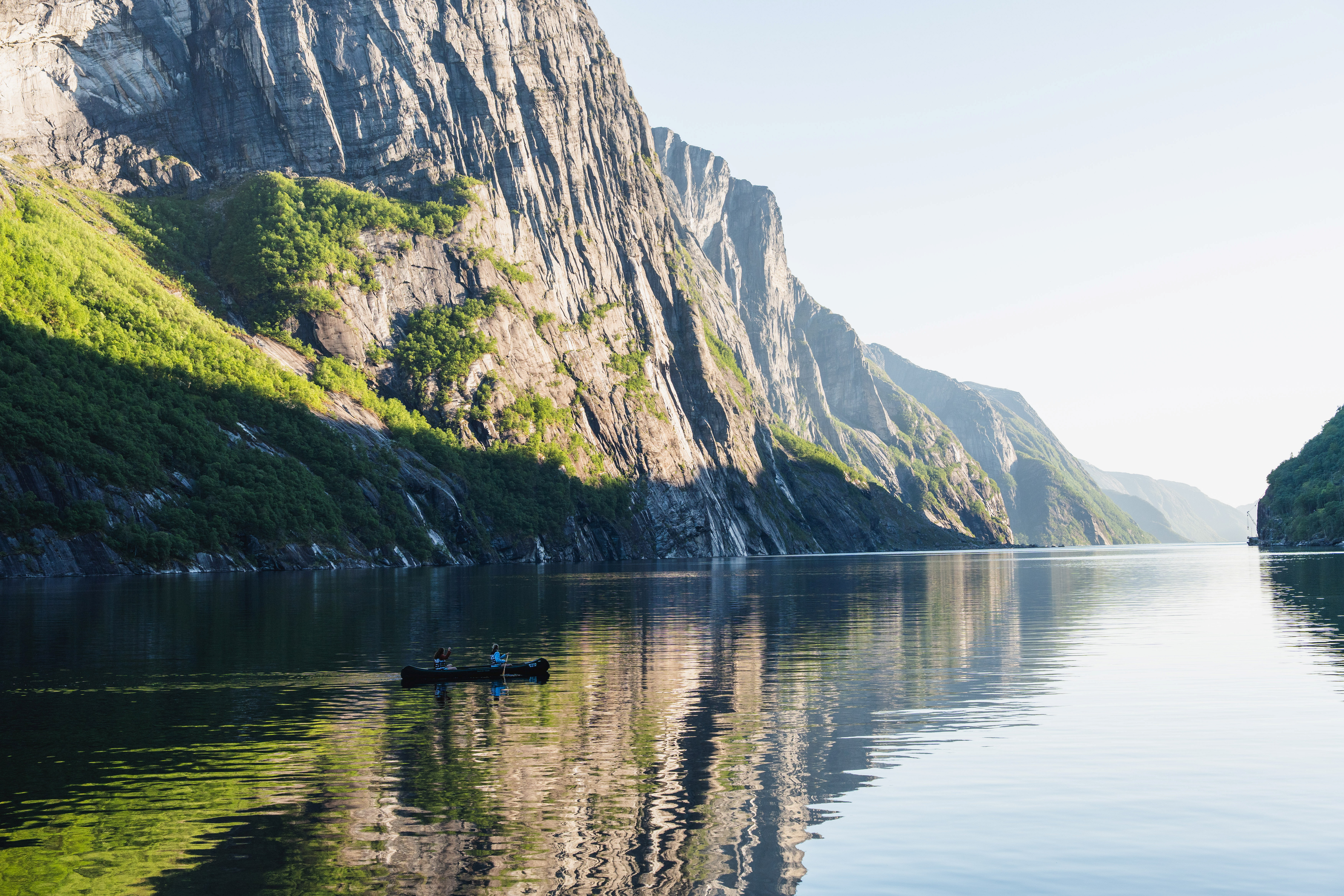 En kano ute p&aring; fjorden med bratte fjellsider.
