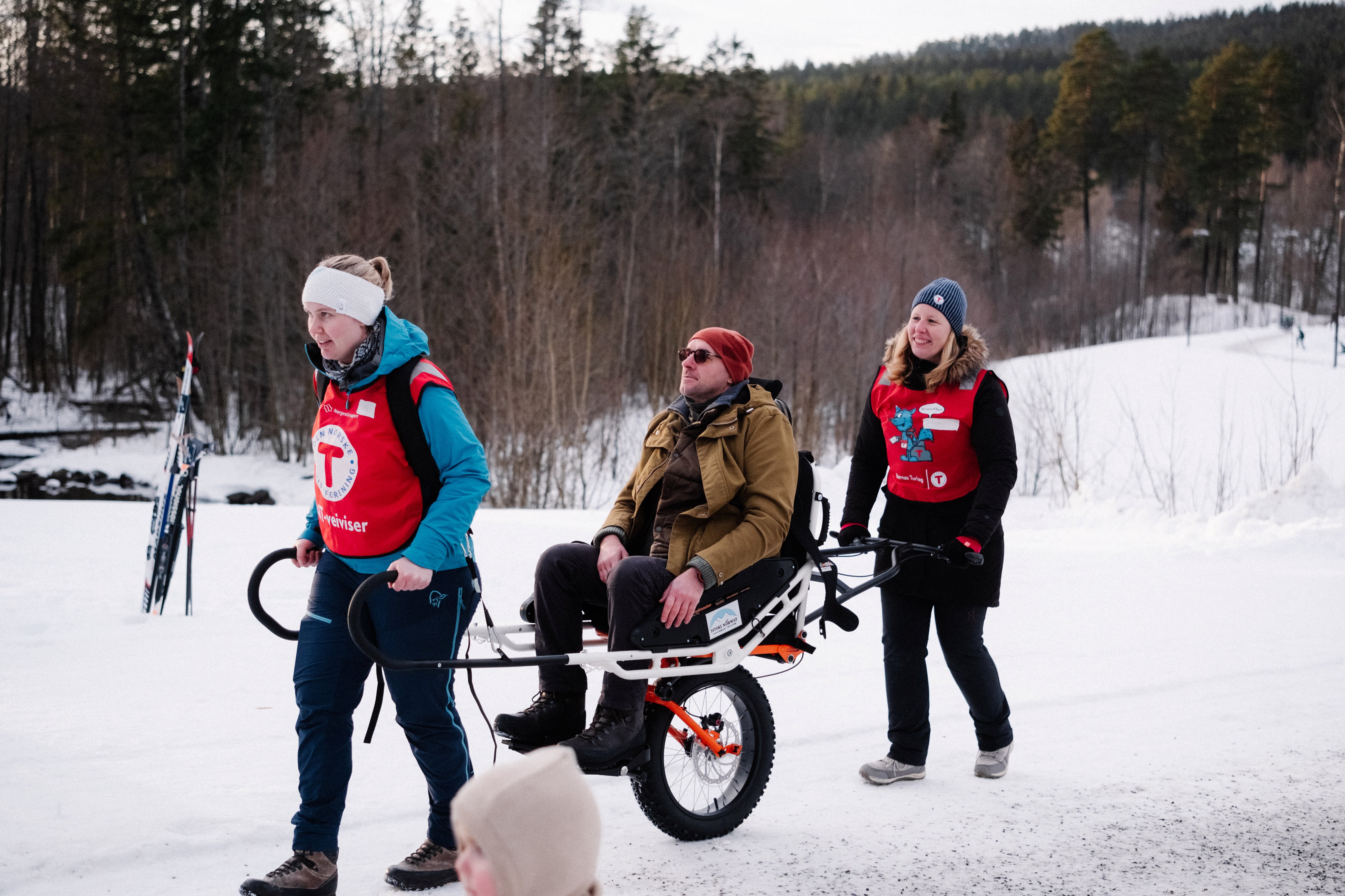 to mennesker triller joelette turvogn med person oppi.
