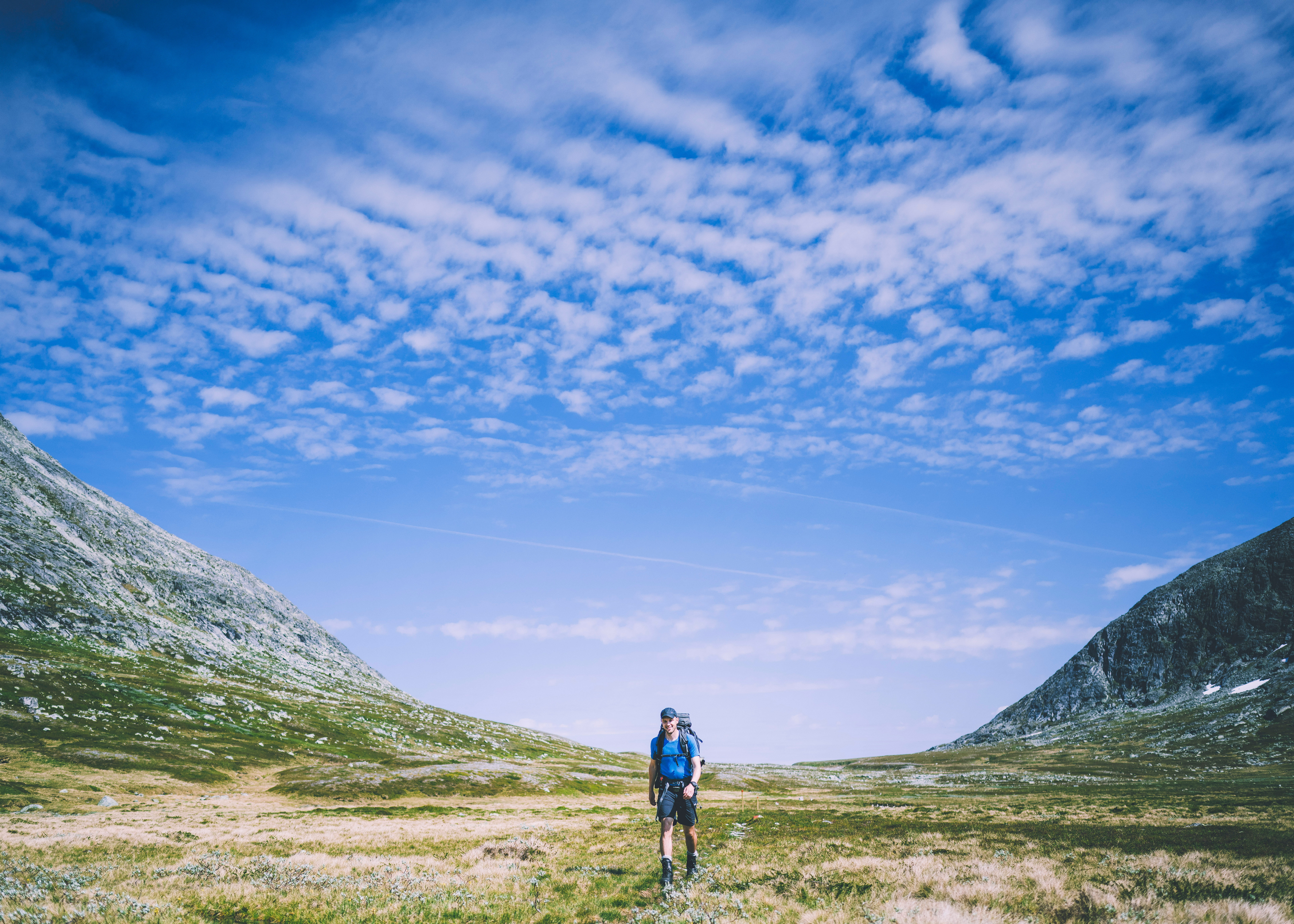en person som g&aring;r p&aring; en sti i en dal med fjell i bakgrunnen
