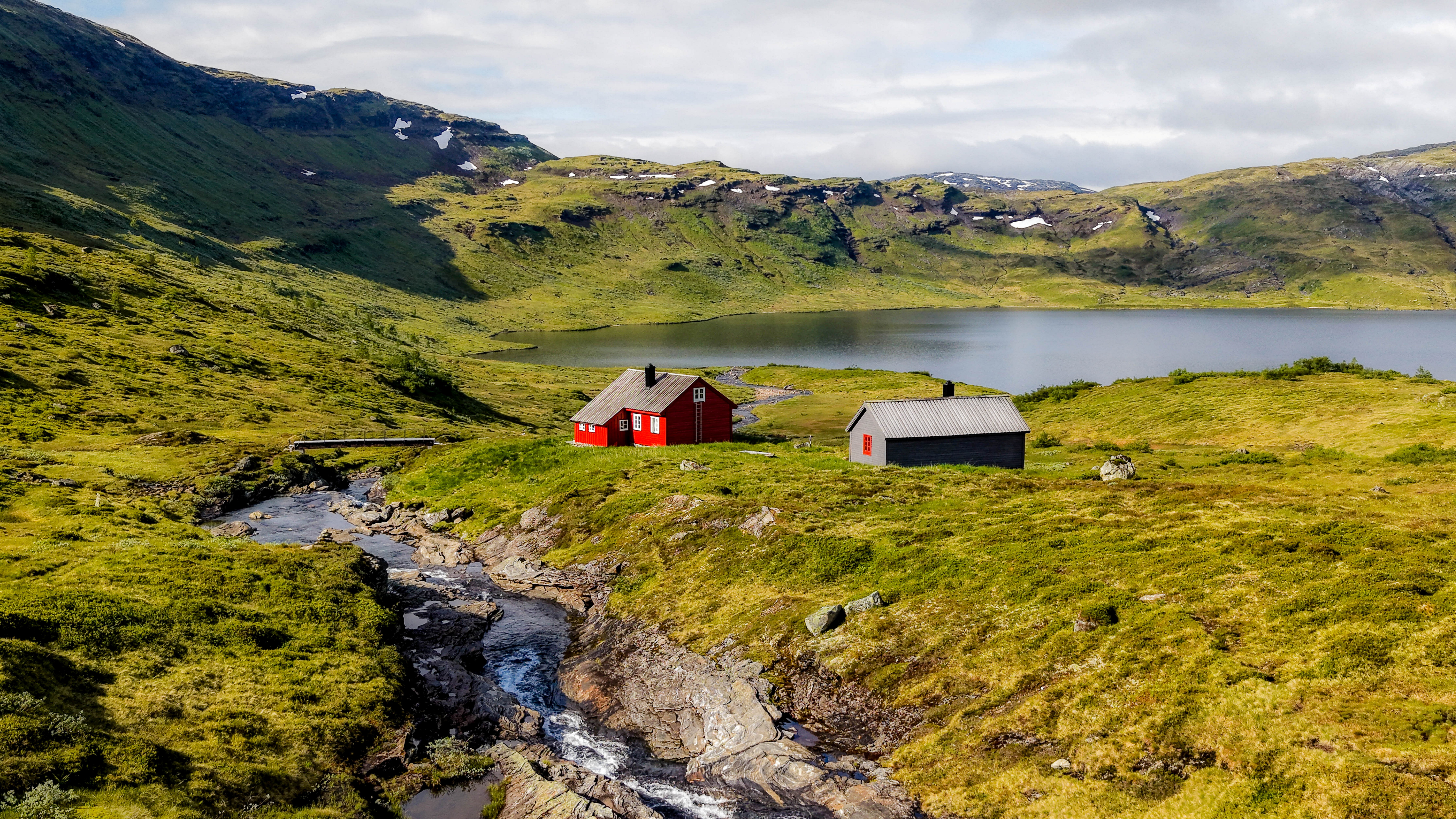 to hytter som ligger i fjellomr&aring;de, ved et vann og en bekk som g&aring;r fra vannet