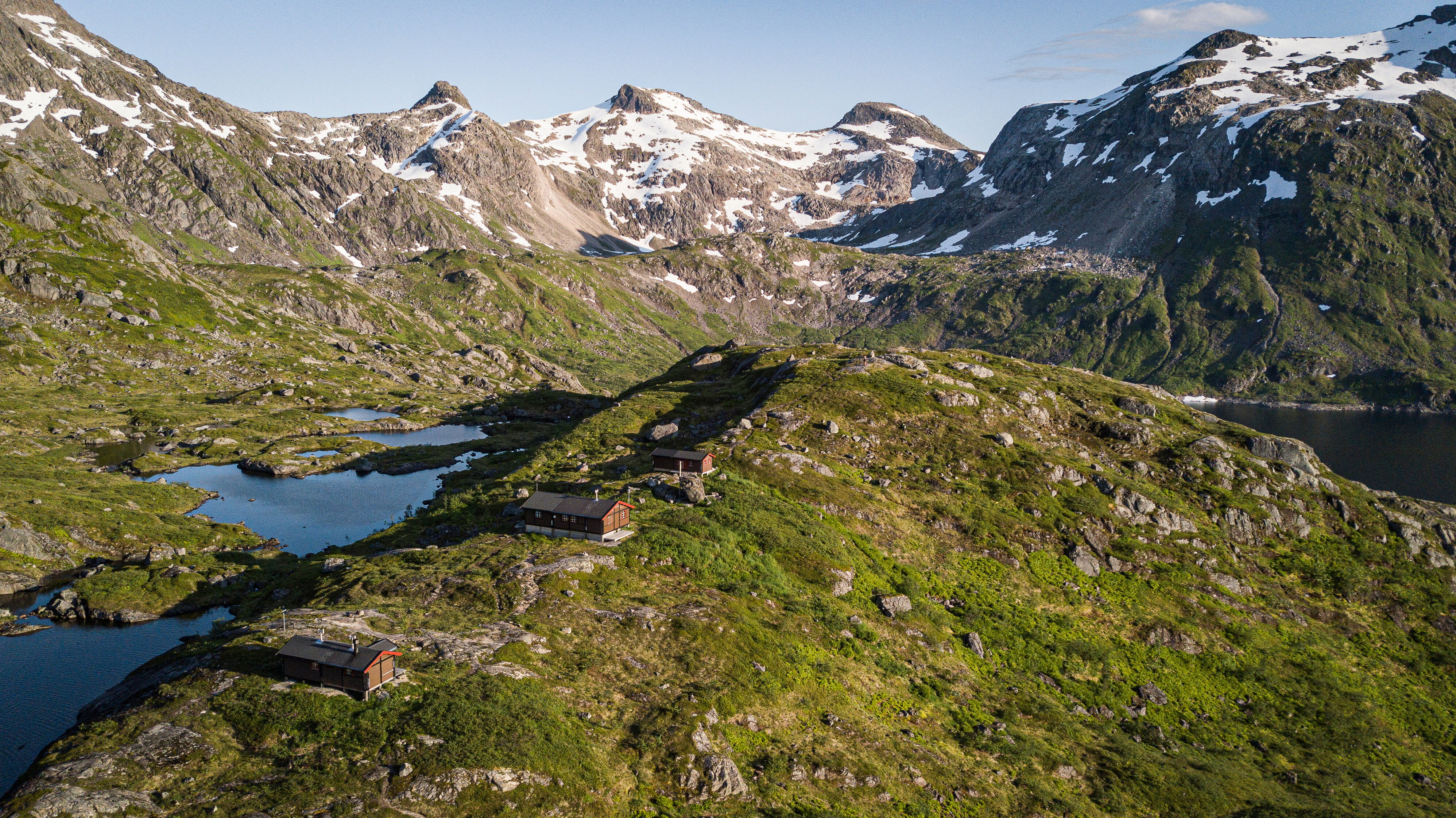 tre hytter som ligger i et mektig fjellandskap med noen sm&aring; vann ved