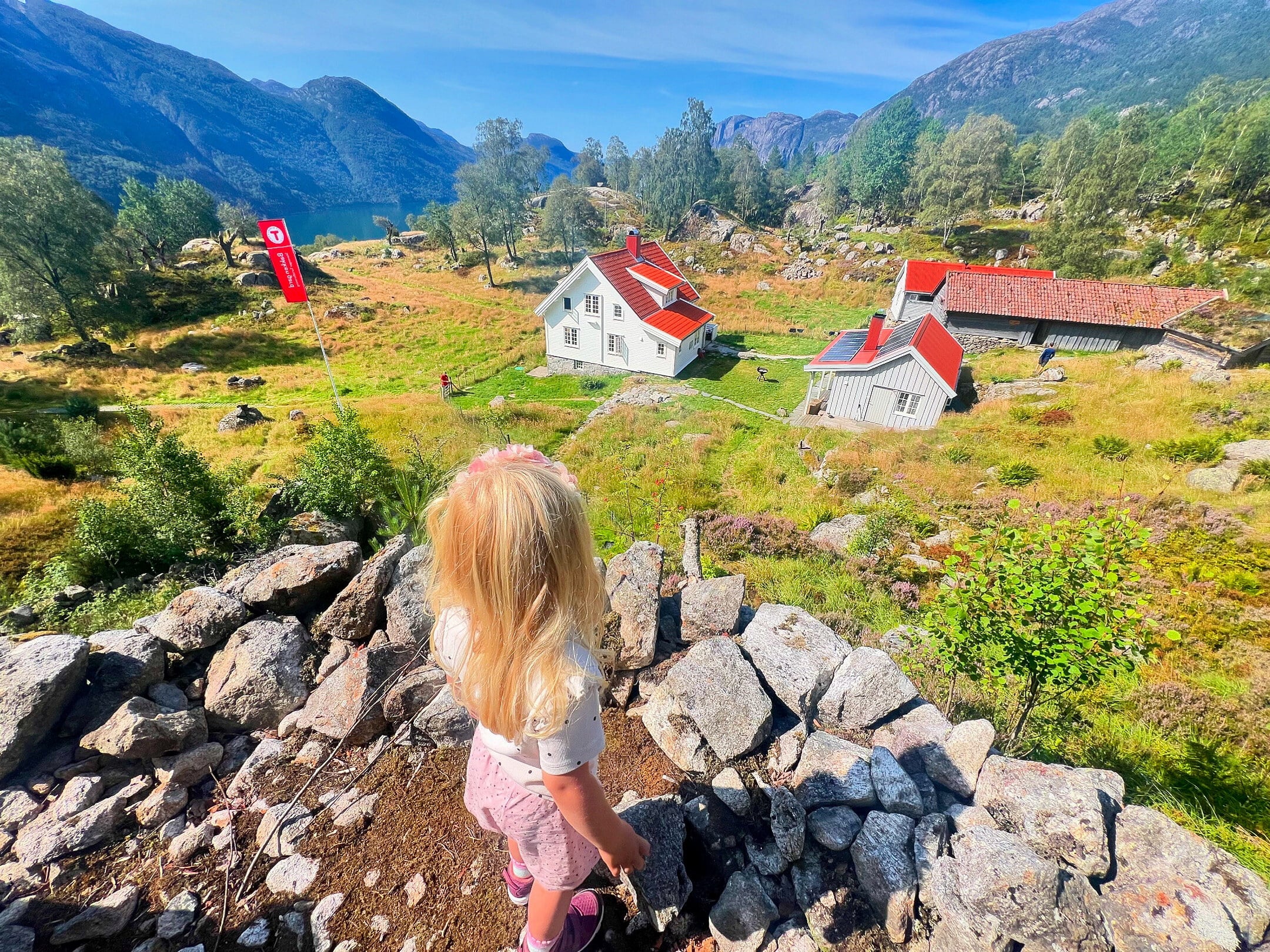 jente ser utover idylliske gr&oslash;nne marker og en liten hvit fjellg&aring;rd 