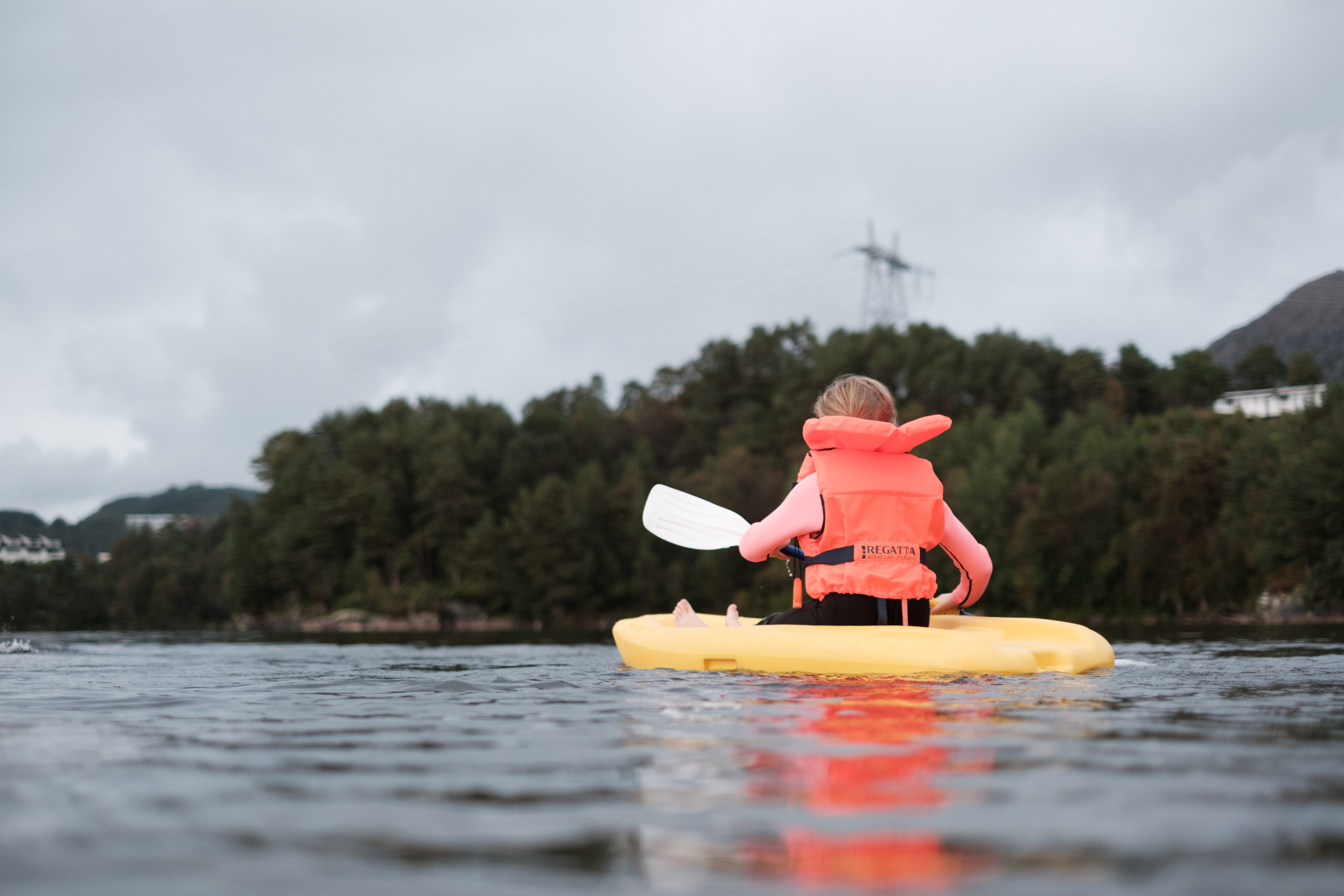 en barn med redningsvest som padler i en liten kajakk p&aring; et vann