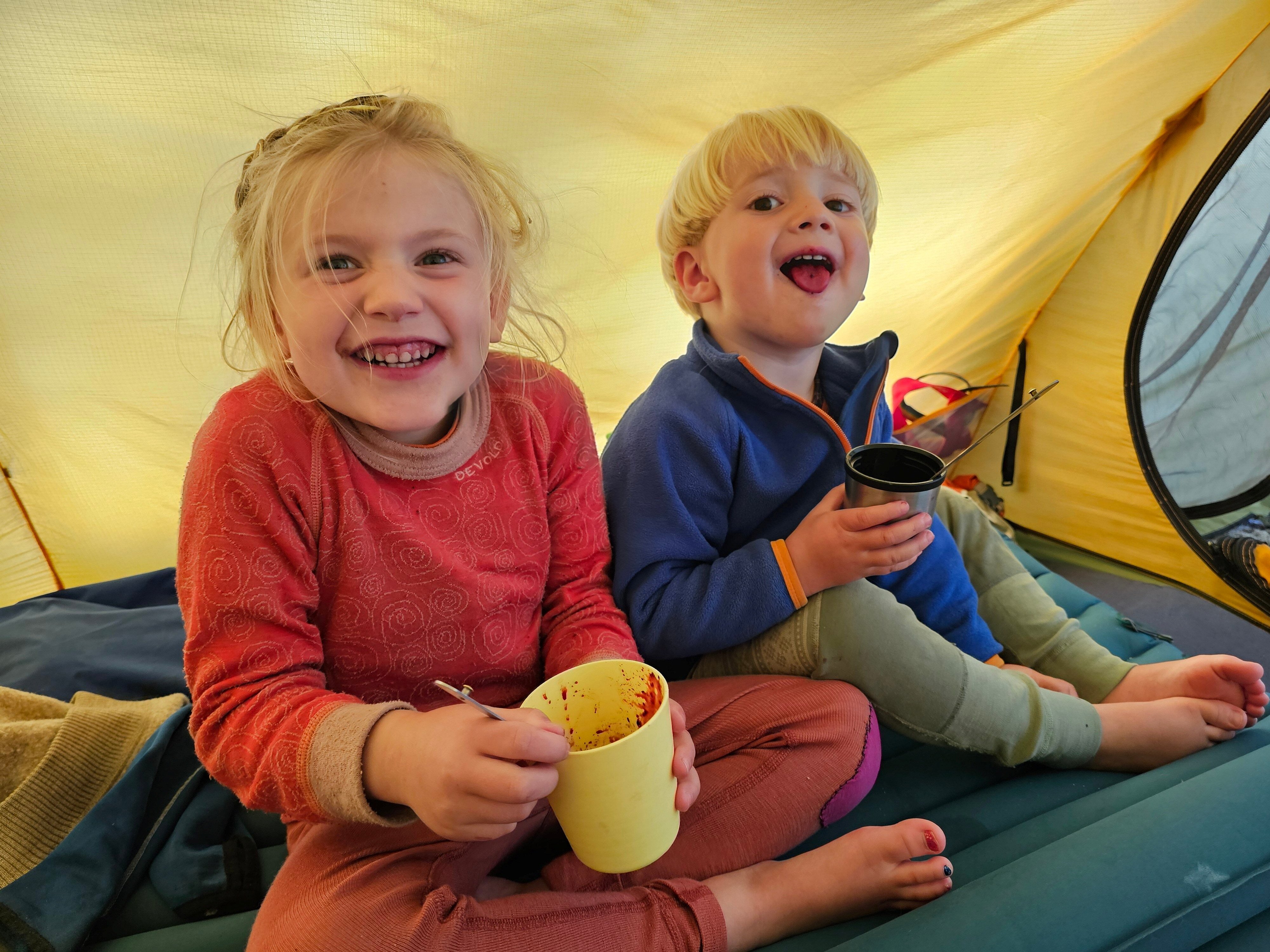 To smilende barn sitter i telt og spiser 
