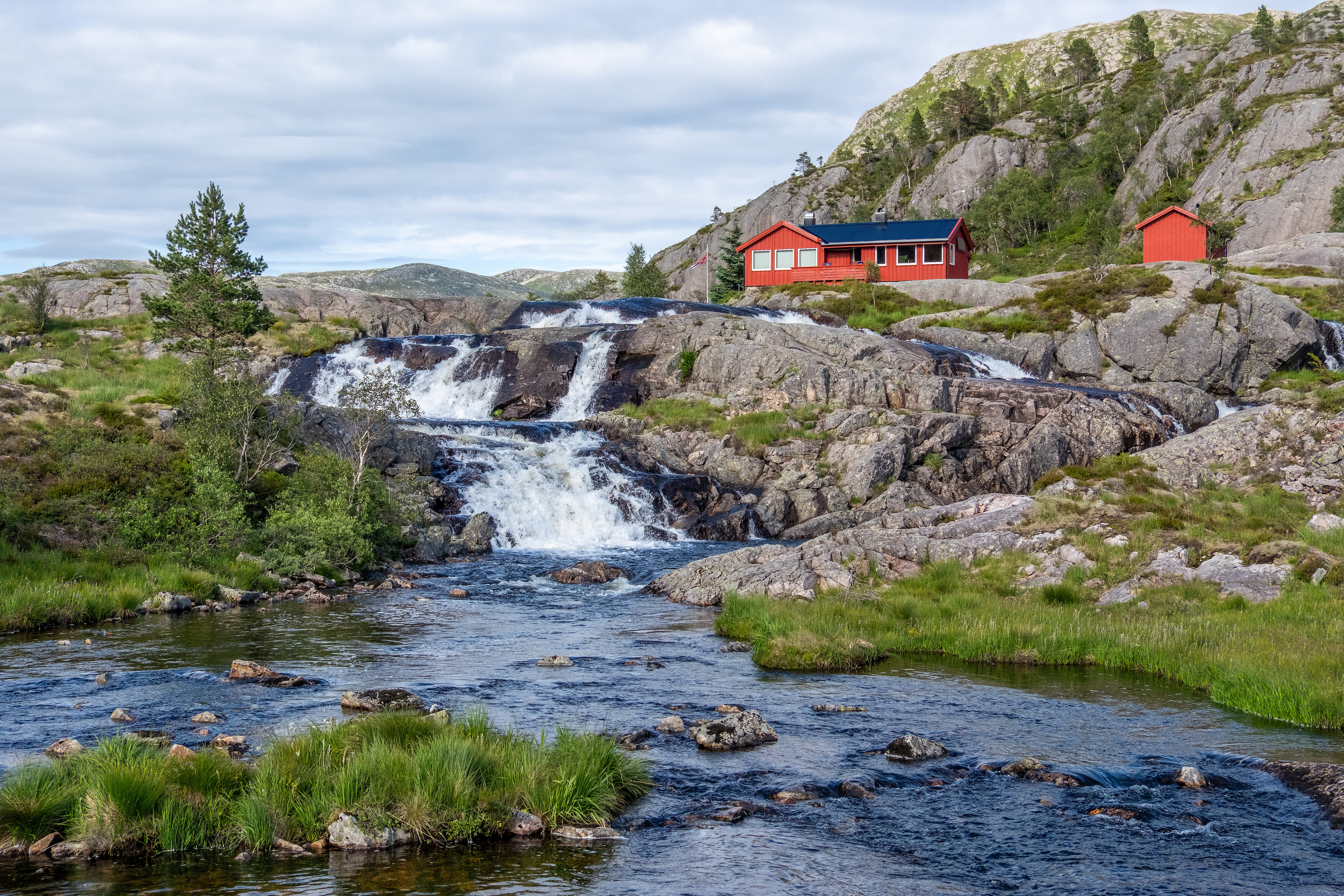 En r&oslash;d hytte med en foss som renner nedenfor.