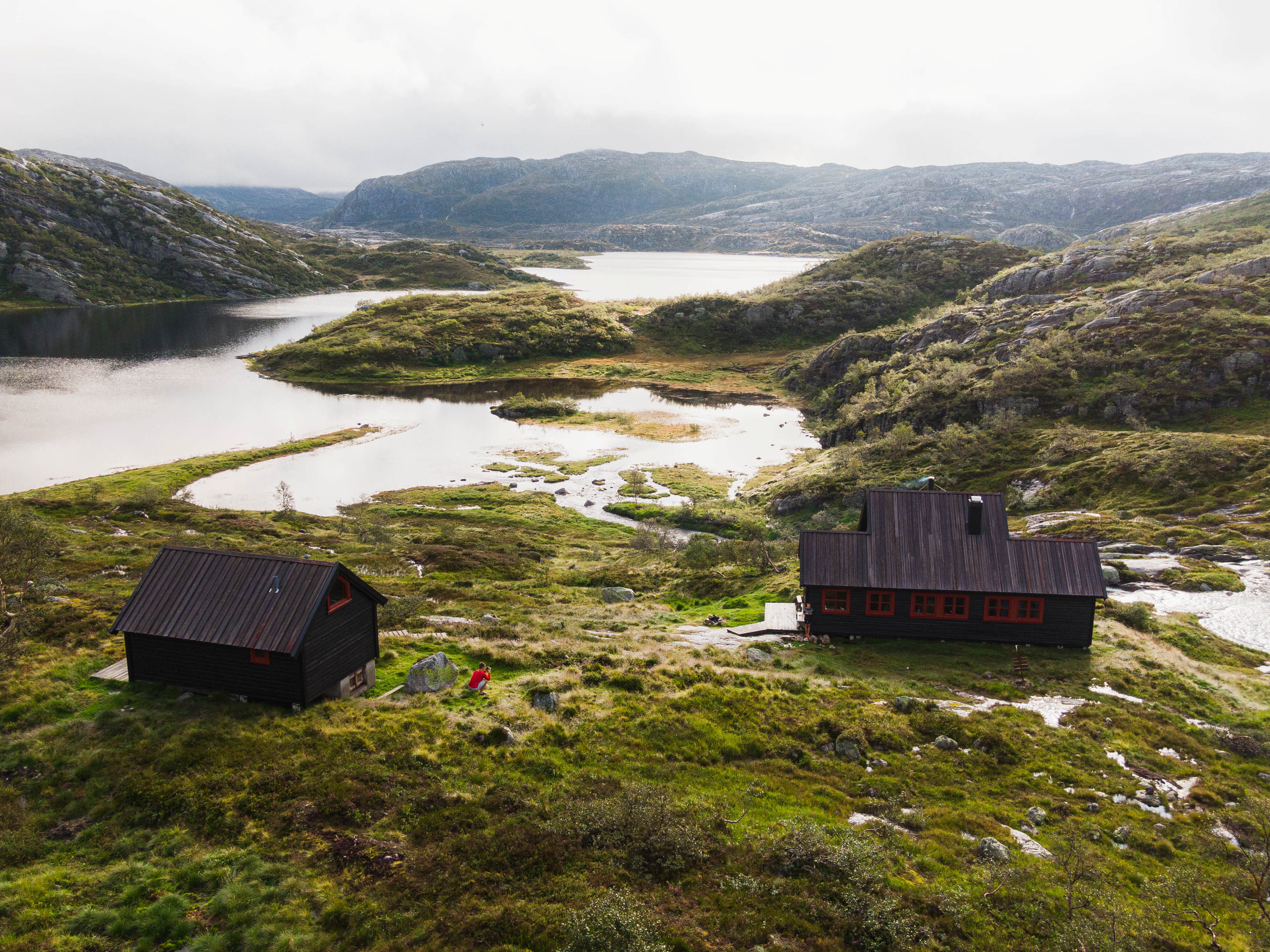 Bilde av en sort hytte som ligger p&aring; en h&oslash;yde over et vann.