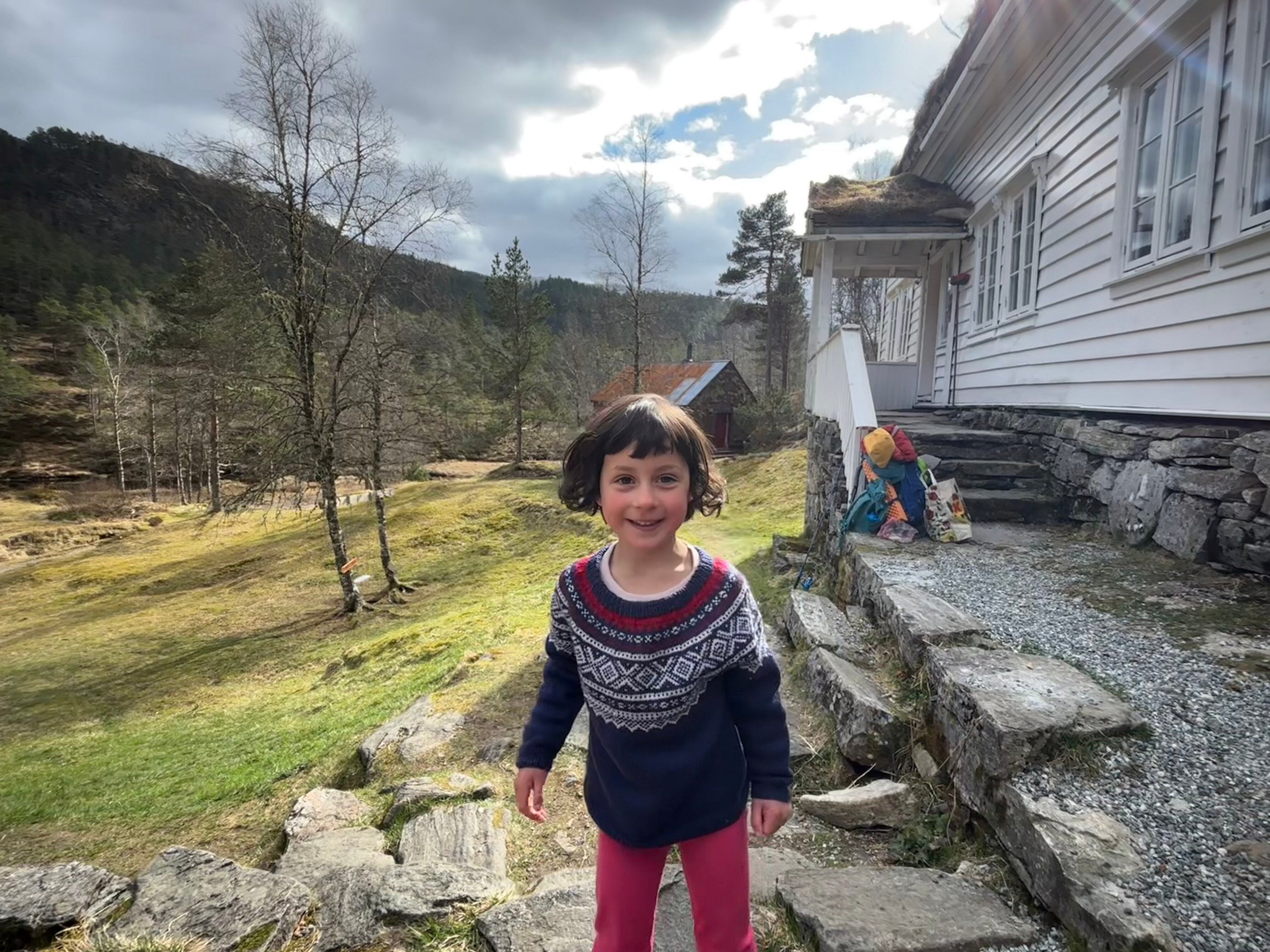 Jente smiler til kameraet foran hyggelig gammel hvit hytte p&aring; landet