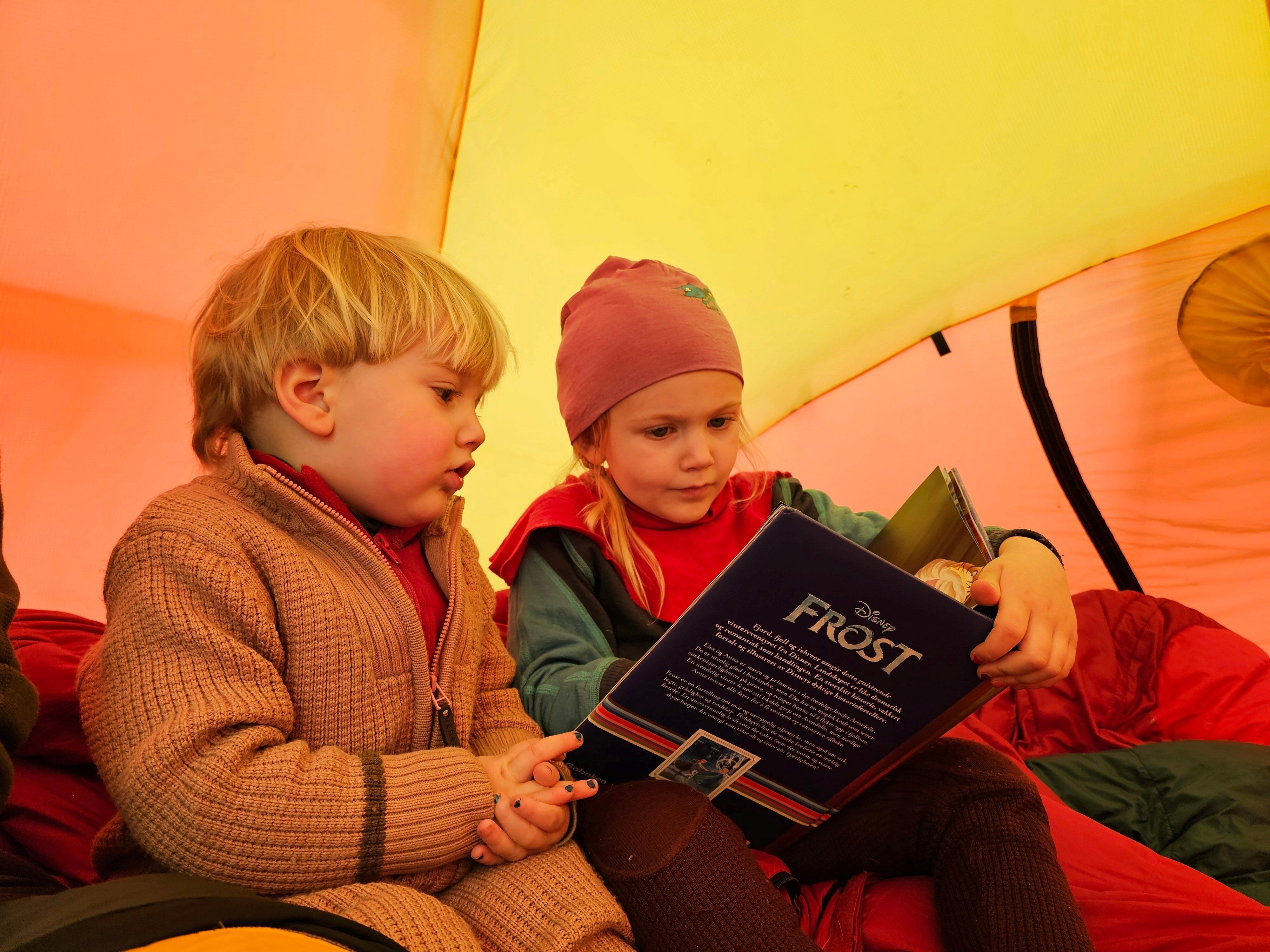 to barn sitter i telt og leser bok