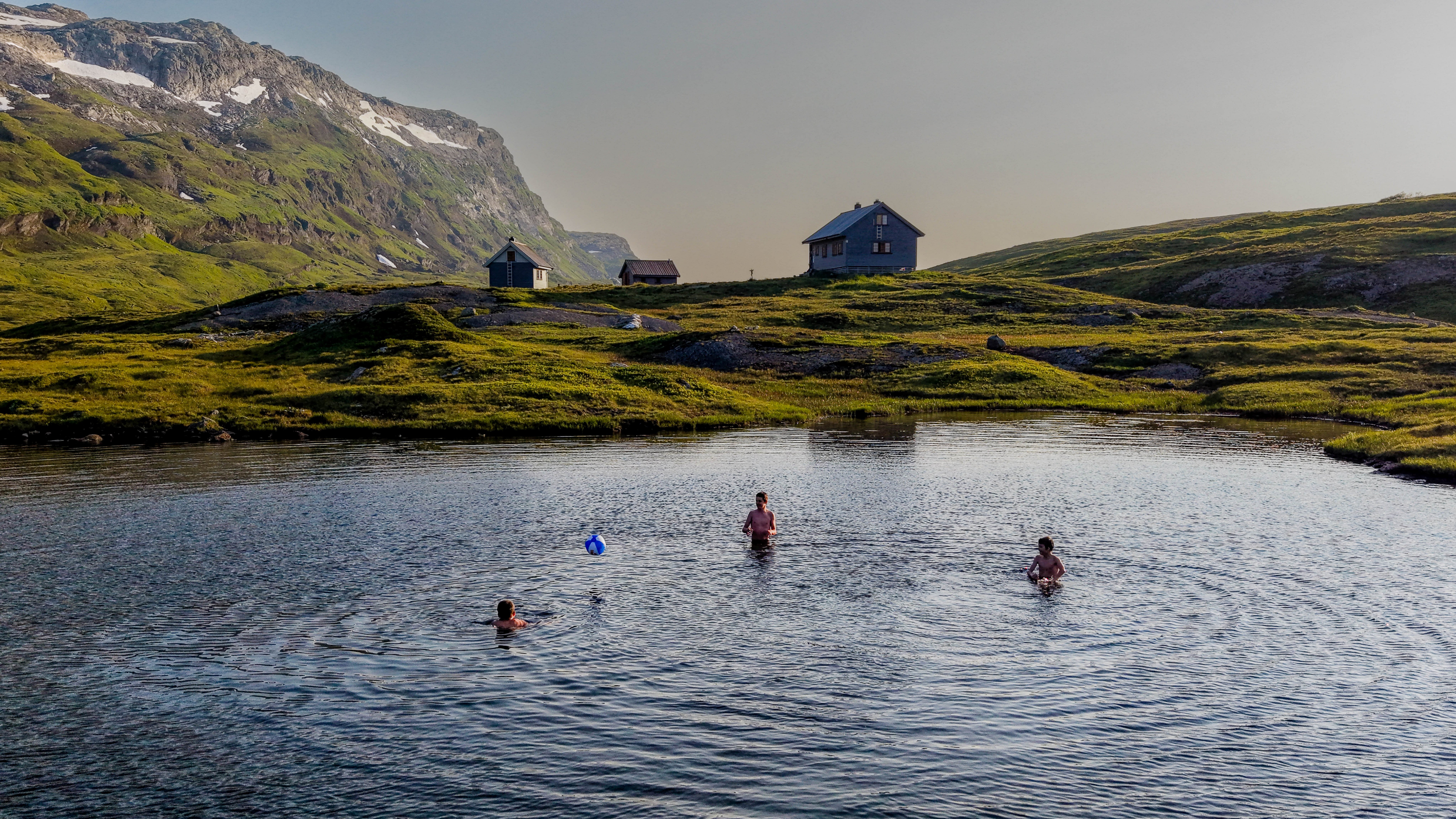 barn leker med ball i fjellvann foran hyttetun