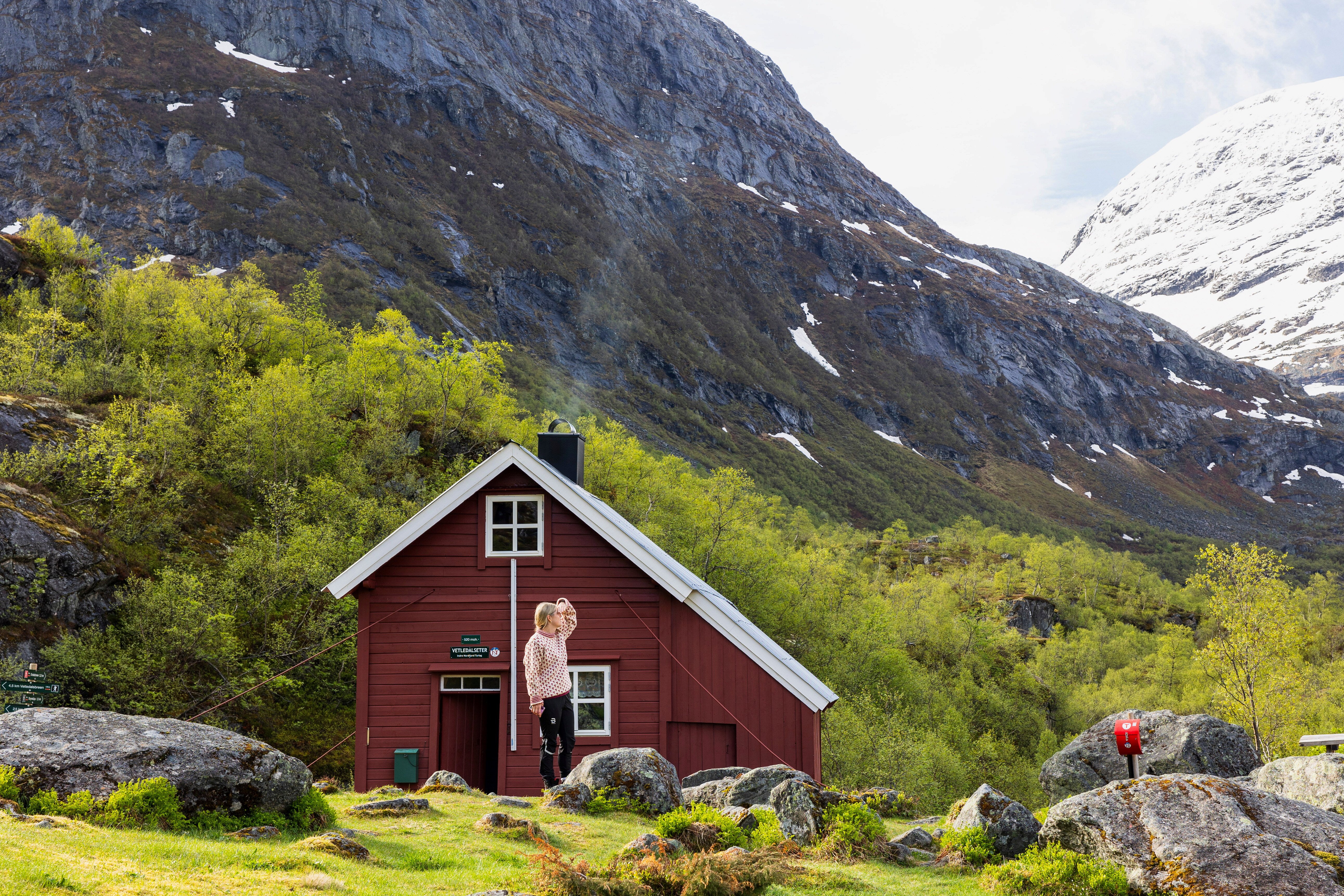 dame ser utover fantastisk landskap med fjell og bre. liten r&oslash;d hytte i bakgrunnen